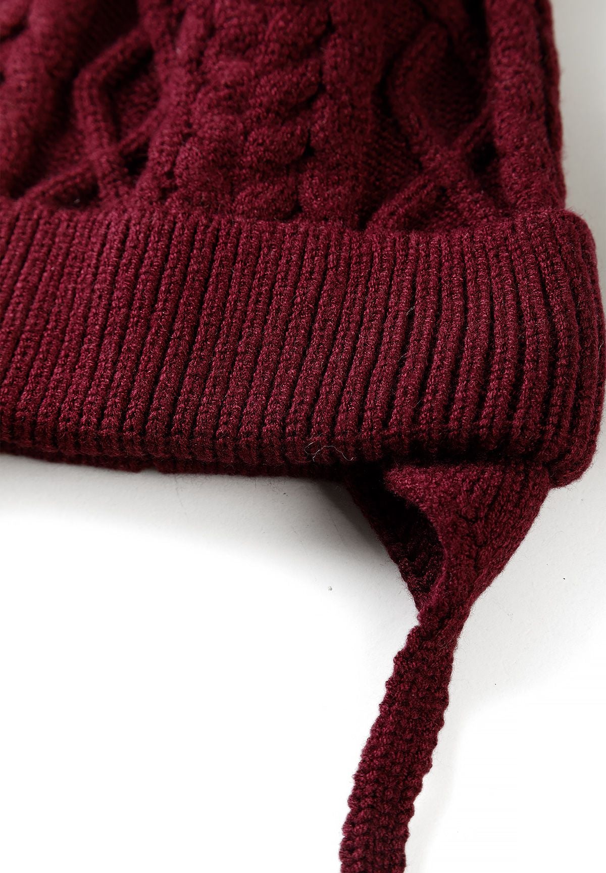 Close-up of the burgundy hat's ribbed folded brim, earflap and knitted chin tie.