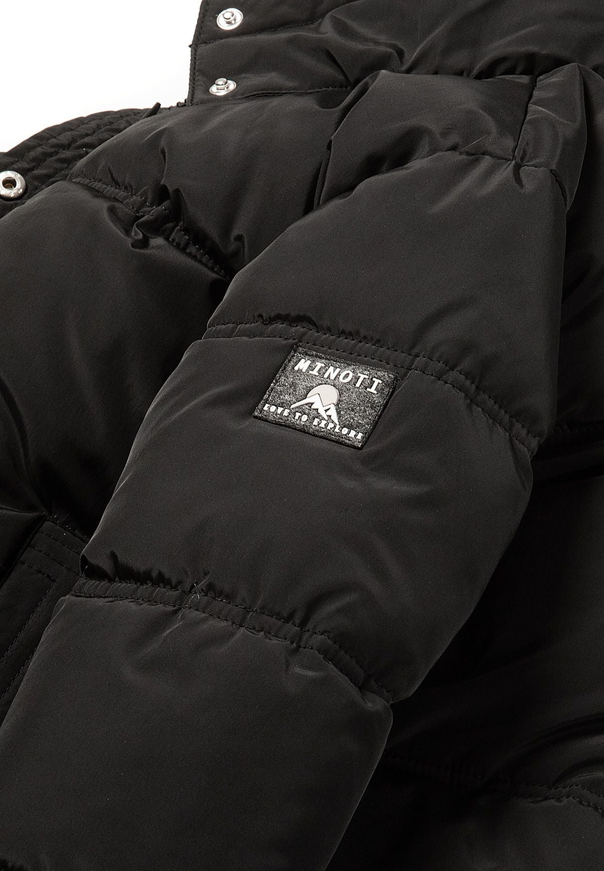 Schwarze Daunenjacke mit Kapuze für Mädchen, Nahaufnahme des Aufnähers am Ärmel.