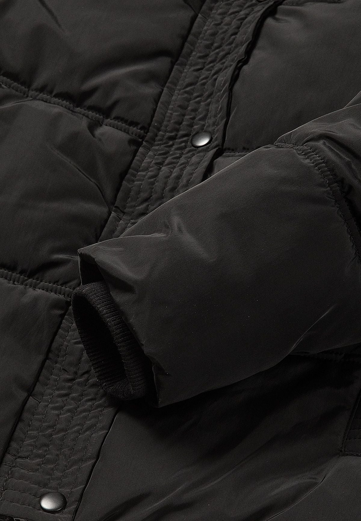 Schwarze Daunenjacke mit Kapuze für Mädchen, Nahaufnahme des gerippten Innenbunds.