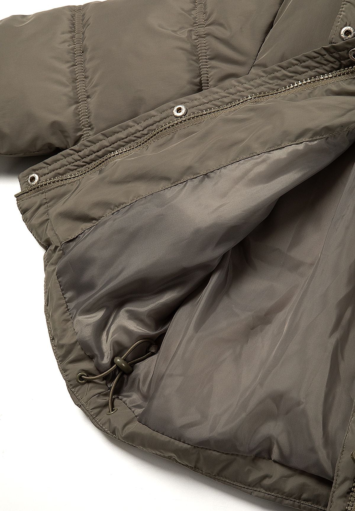 Inside view of smooth khaki lining and a cord toggle near the hem of the padded jacket.