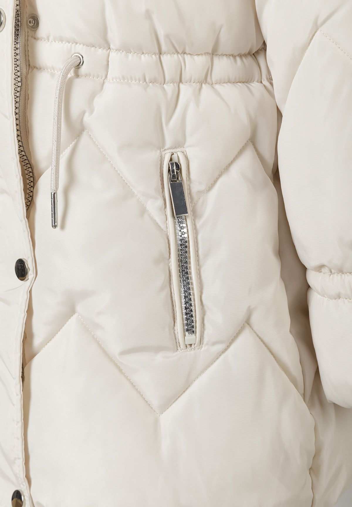 Close-up of a slanted zip pocket beside the cream coat's waist drawcord and chevron quilting.
