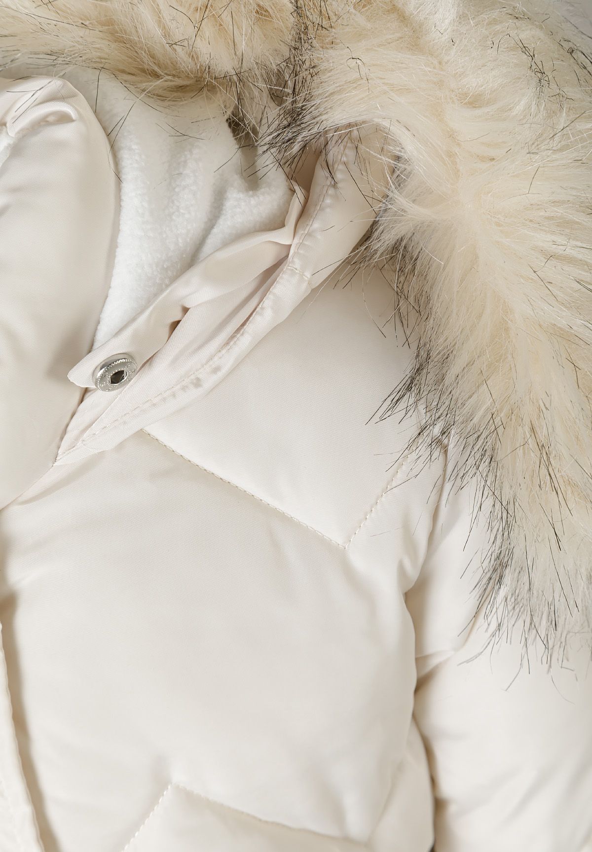 Close-up of the cream coat's fluffy hood trim, white inner lining and snap-fastened collar.