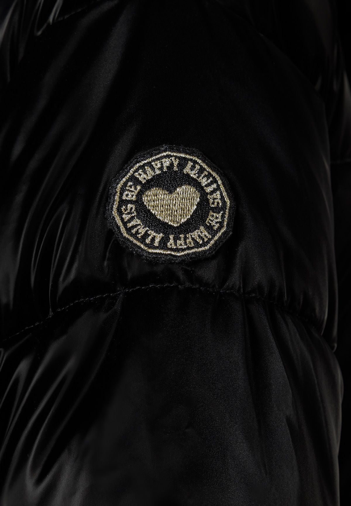 Close-up of a round black and gold heart badge on a glossy black puffer sleeve.