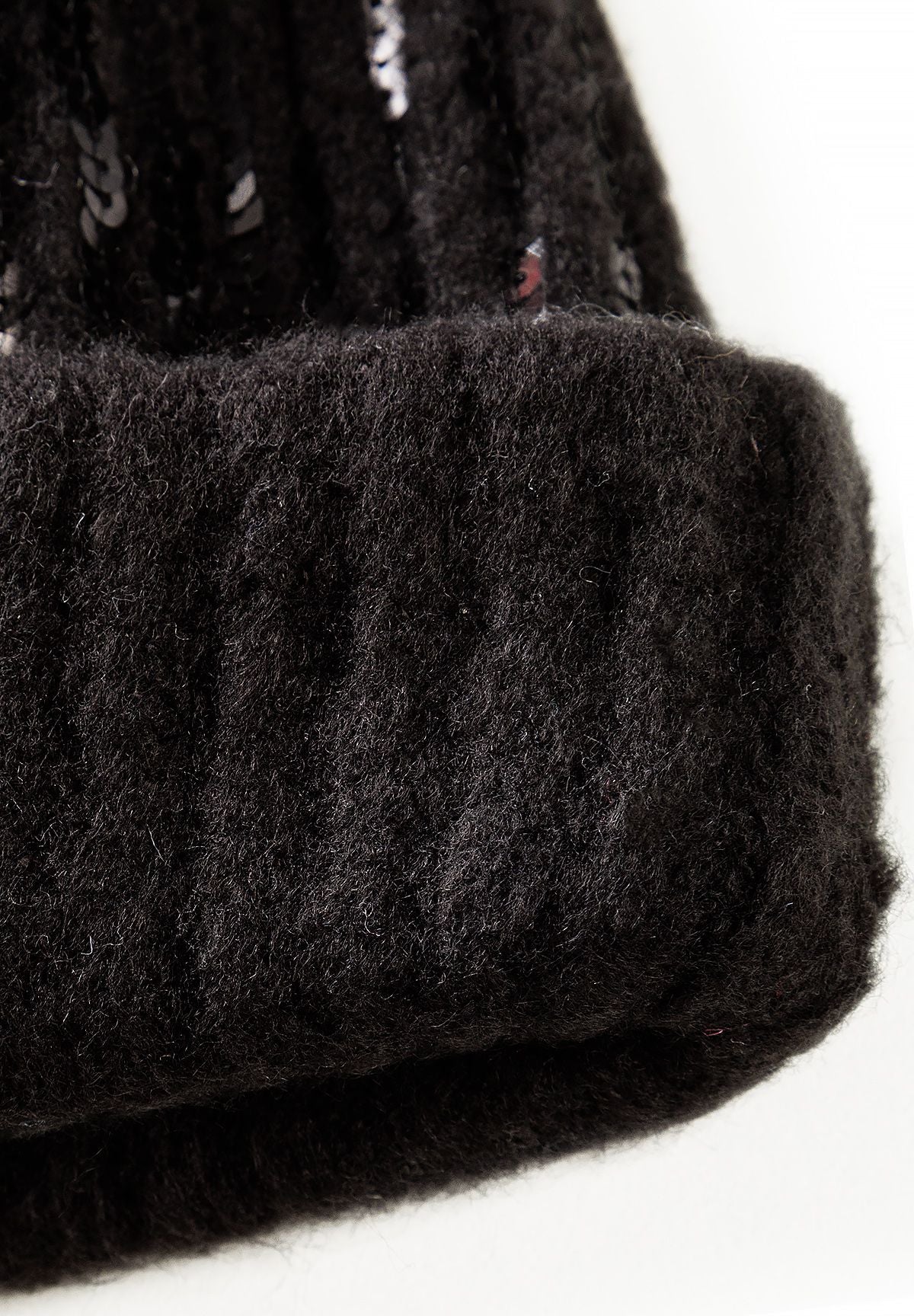 Close-up of black rib-knit beanie's plain folded cuff below sequin rows.