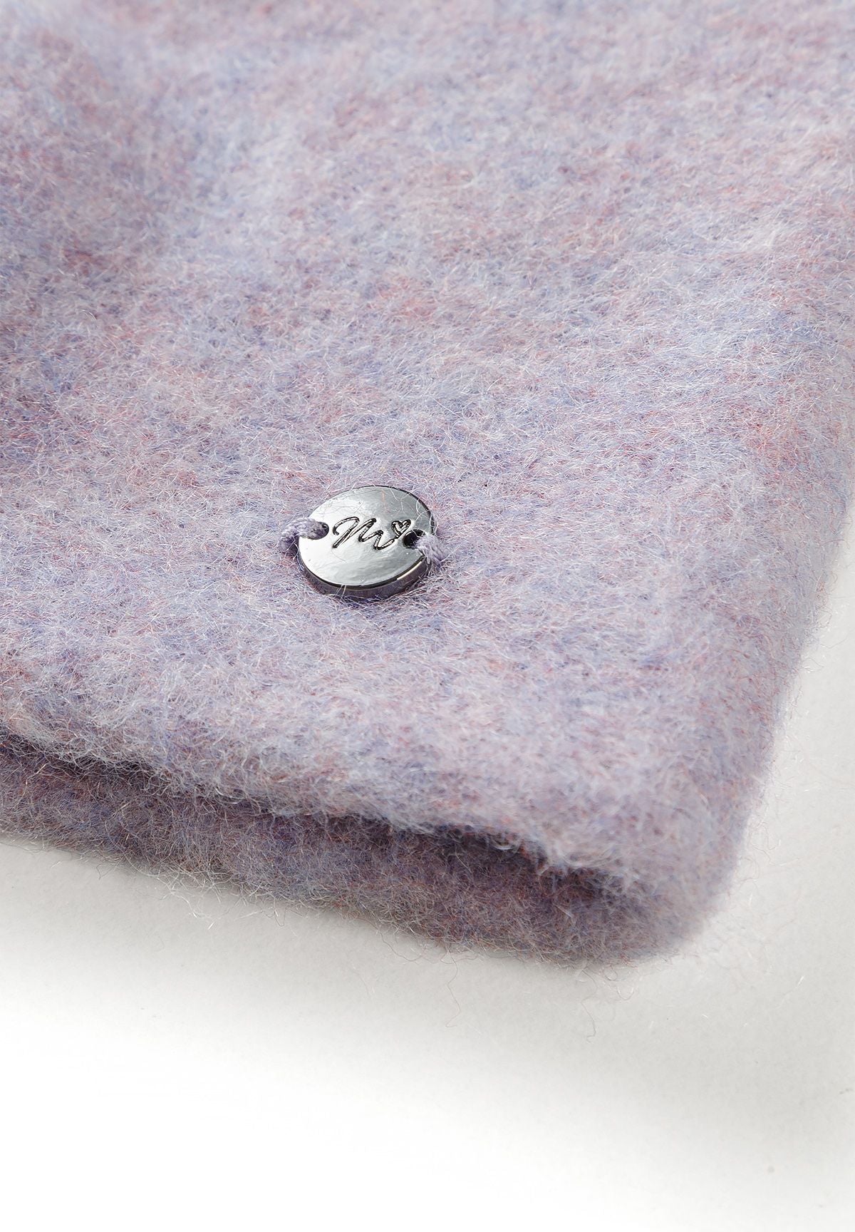 Close-up of a small round silver-tone logo badge on lilac fuzzy headband fabric.