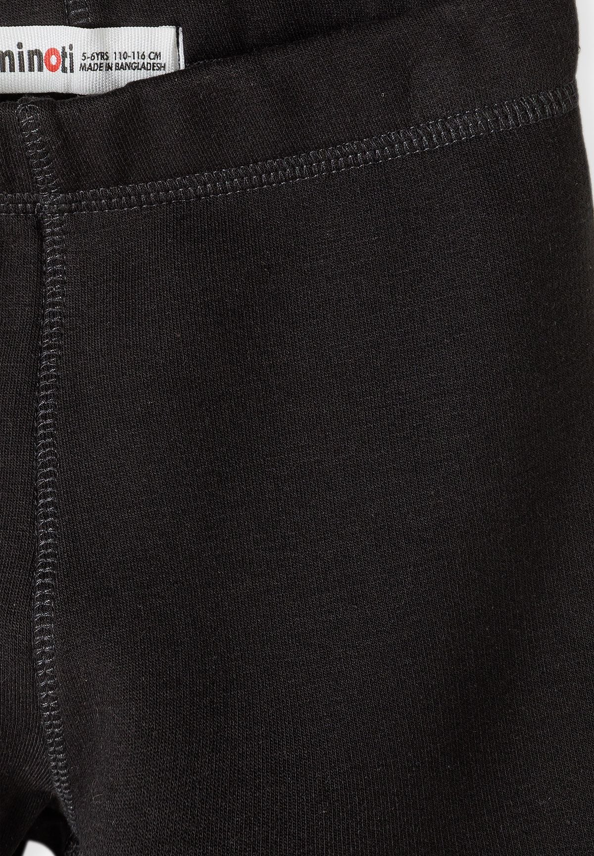 Close-up of black leggings waistband with visible knit texture, stitching and Minoti label.