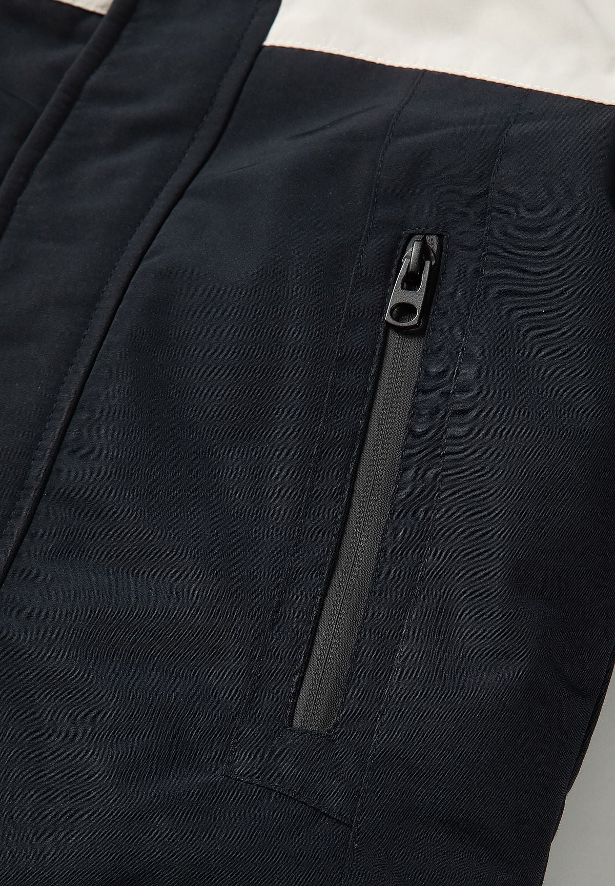 Long vertical black hip-pocket zip on the parka's dark lower front beneath a cream panel.