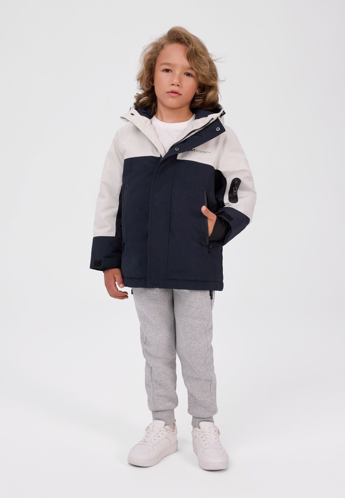 Boy wearing a cream and black colour-block parka with a hood and a black zipped sleeve pocket.