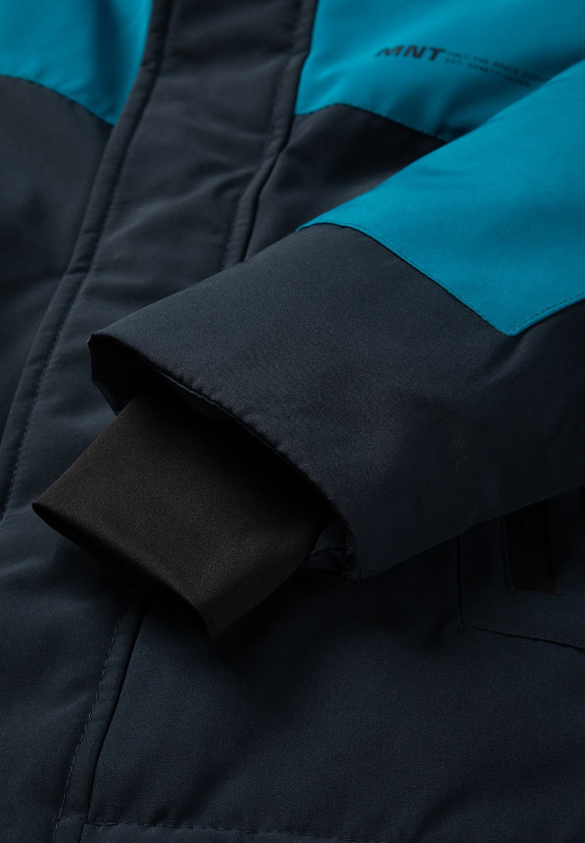 Layered navy parka cuff with a dark ribbed inner sleeve beneath a teal upper panel.
