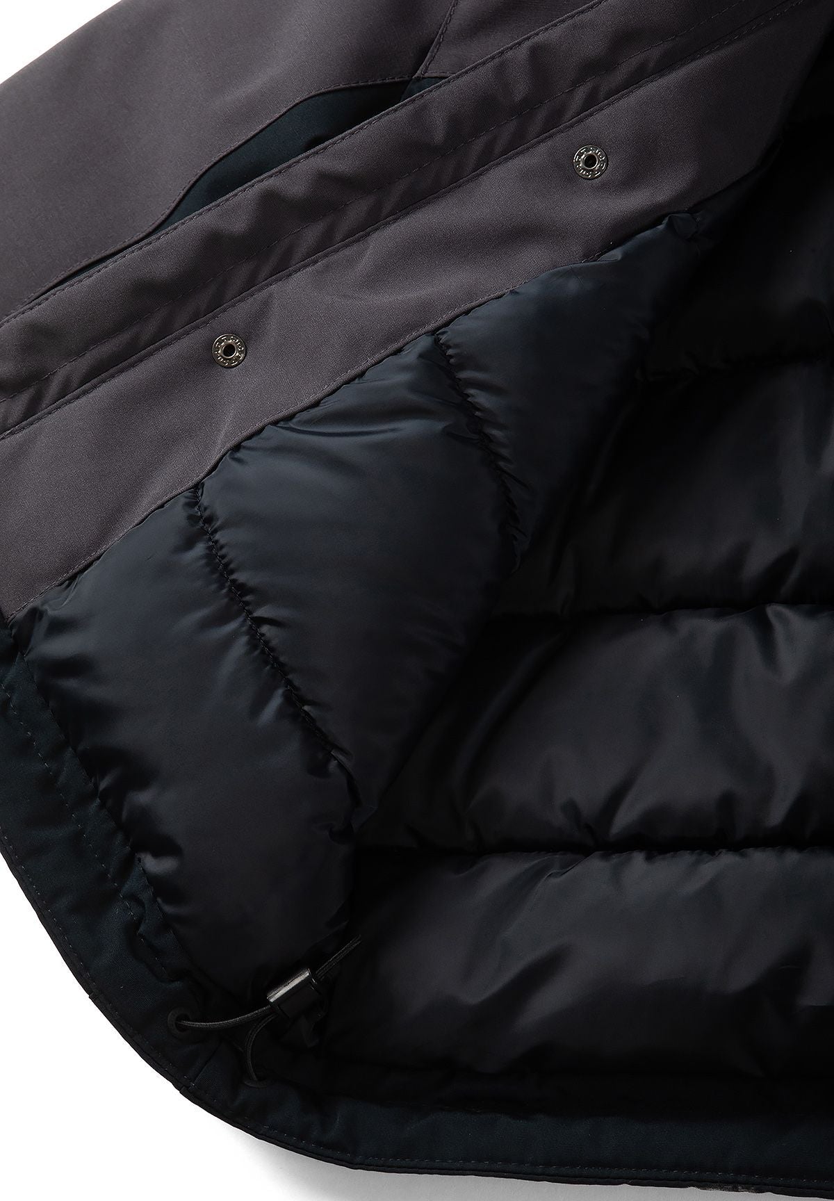 Inside of the charcoal and black parka showing black quilted lining beside its snap-fastened placket.