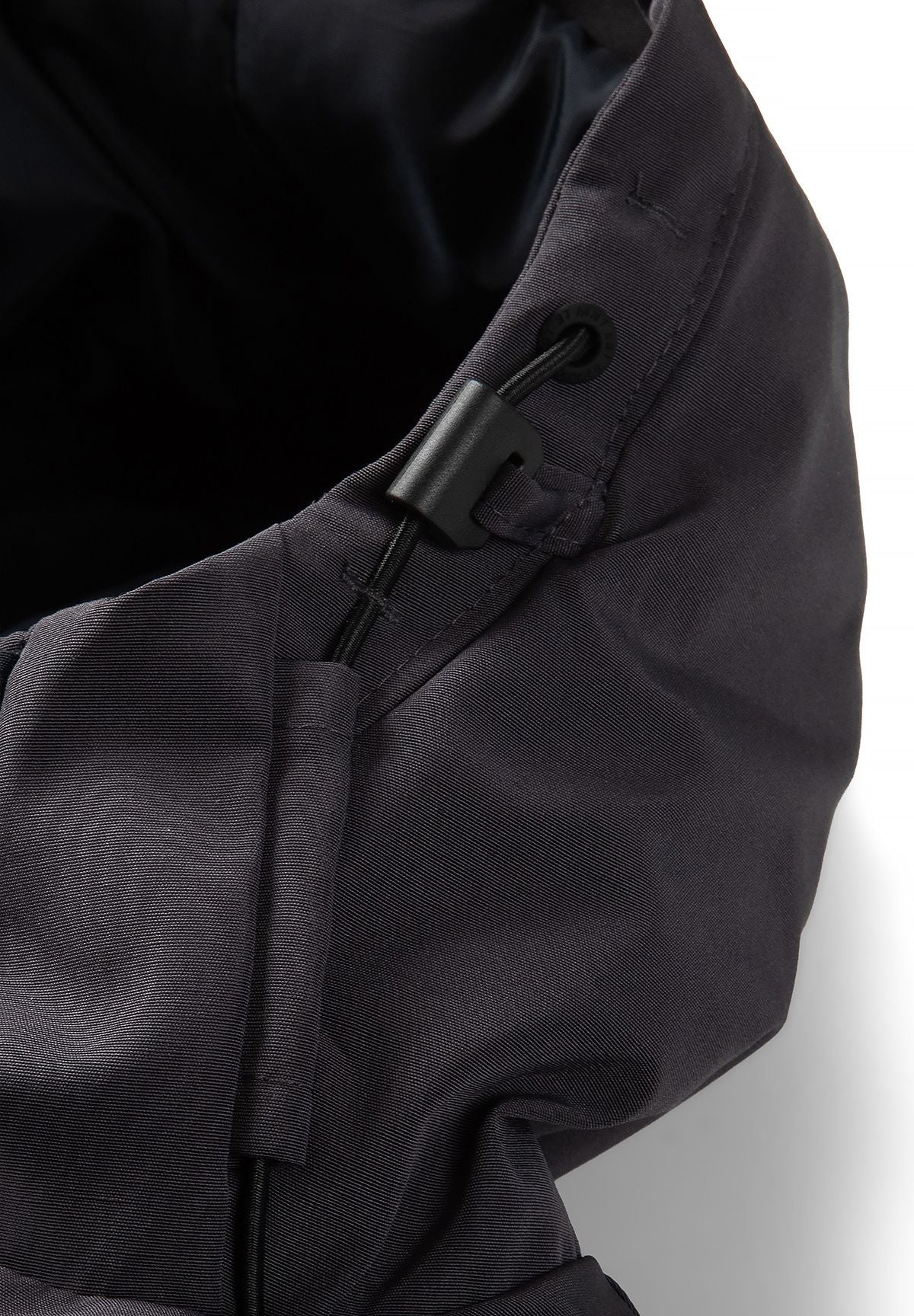 Close-up of the parka hood's black drawcord, eyelet and sliding adjuster on charcoal fabric.