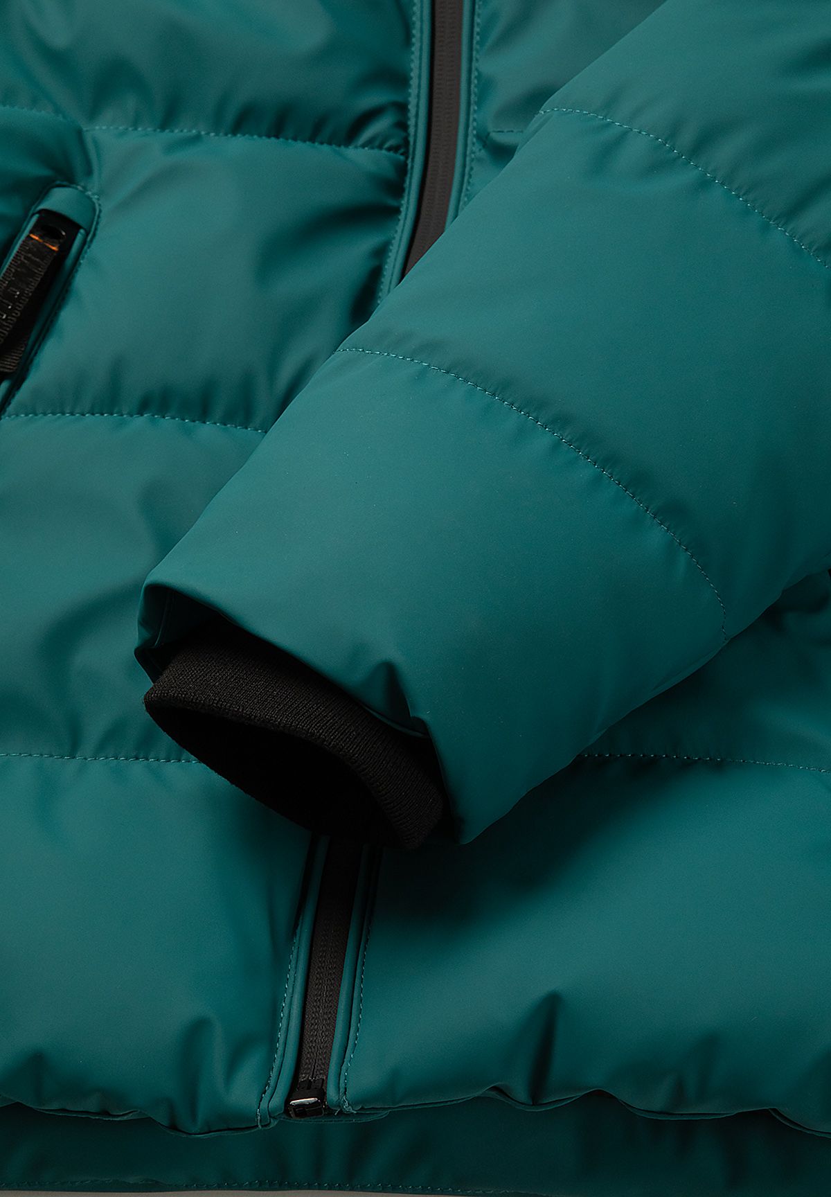 Close-up of a black ribbed inner cuff beneath the teal padded sleeve of the jacket.