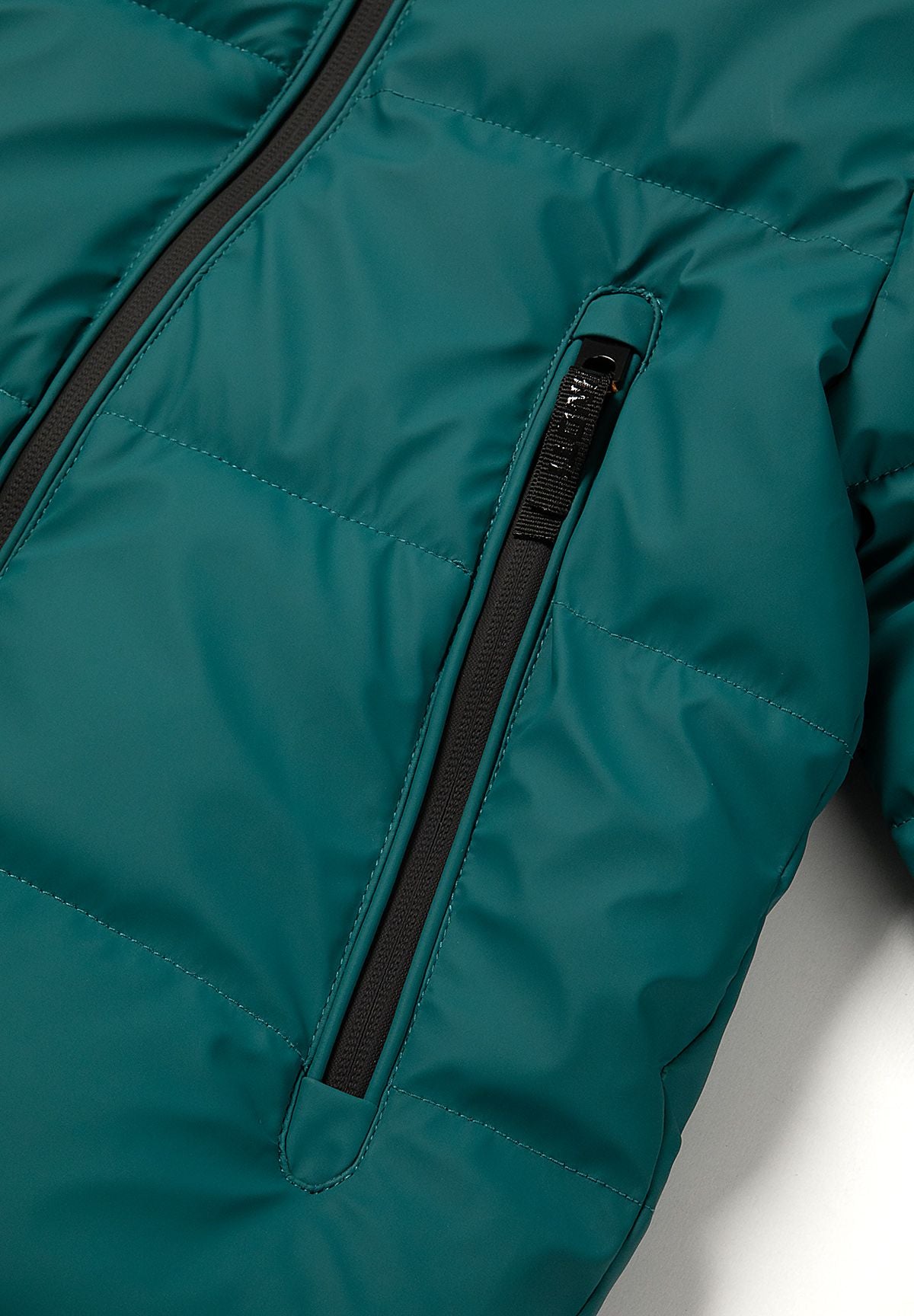 Close-up of a long vertical black zipped pocket on the teal padded jacket front.