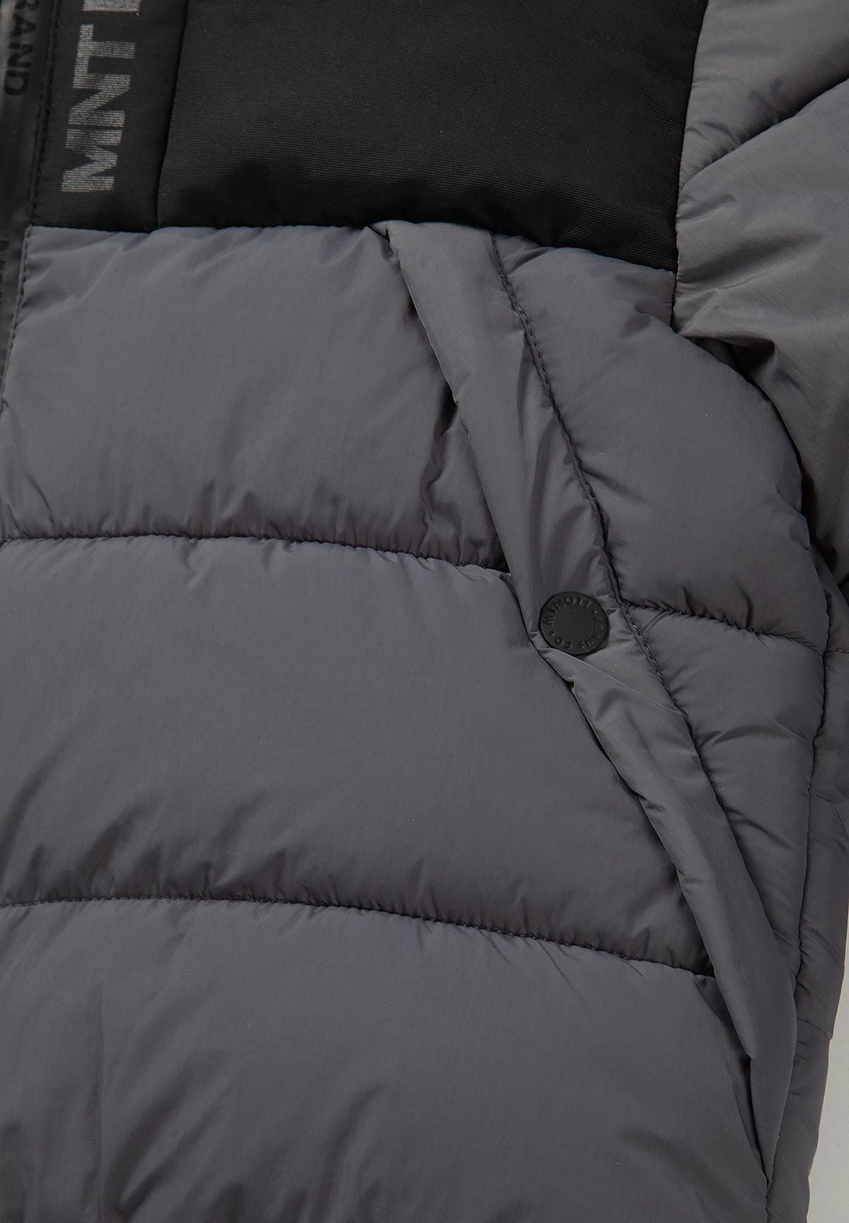 Close-up of a slanted grey pocket opening with black snap on the quilted puffer jacket.
