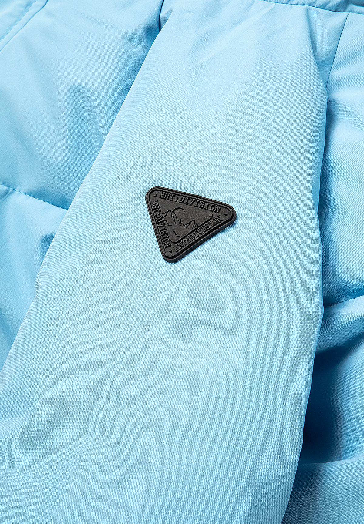 Lichtblauwe en marineblauwe gewatteerde parka met kleurblokken voor jongens, detail van het embleem op de borst.