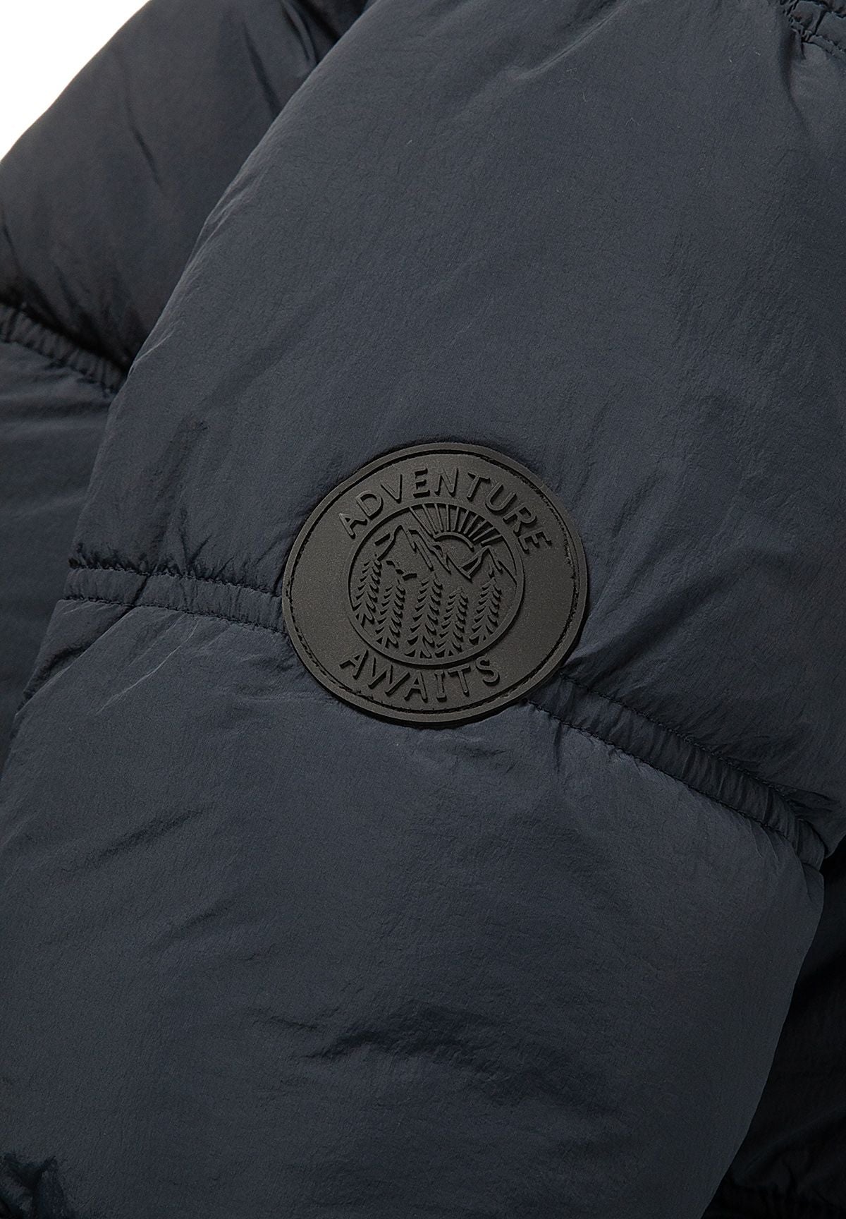 Piumino da ragazzo blu navy con cappuccio, primo piano del distintivo sulla manica.