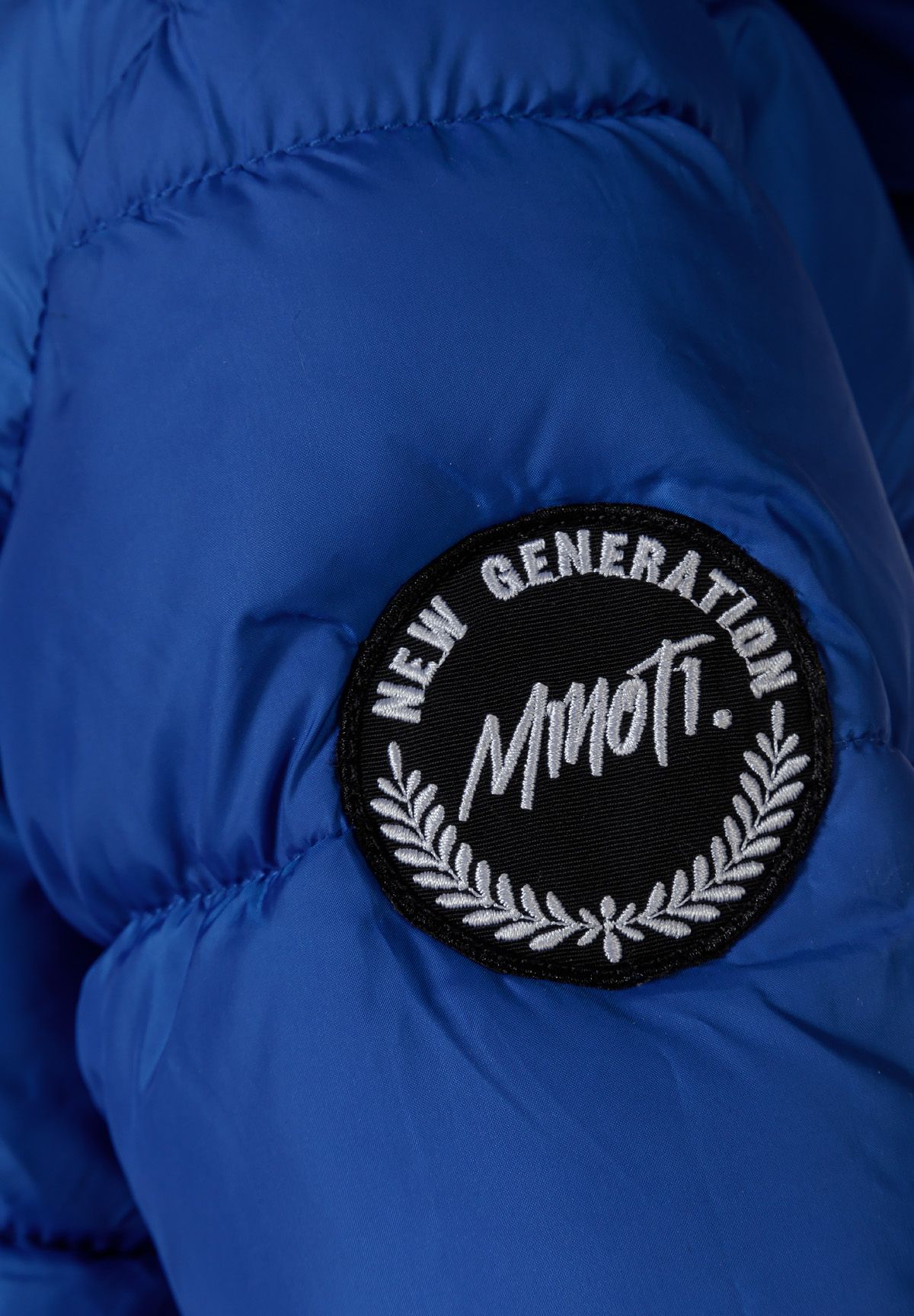 Close-up of the black NEW GENERATION MINOTI sleeve patch on a royal blue quilted parka.