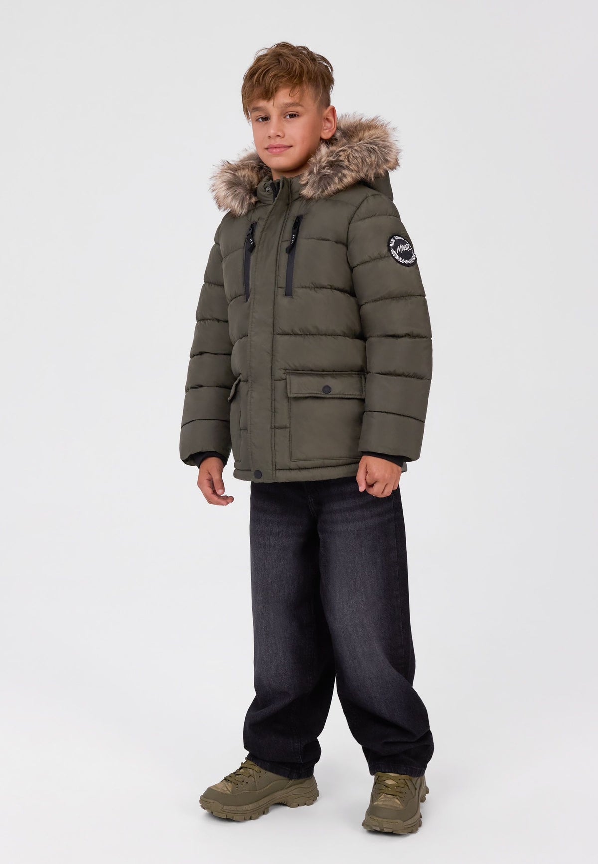 Boy wearing an olive khaki quilted parka with fur-look hood, zipped chest pockets and lower flap pockets.
