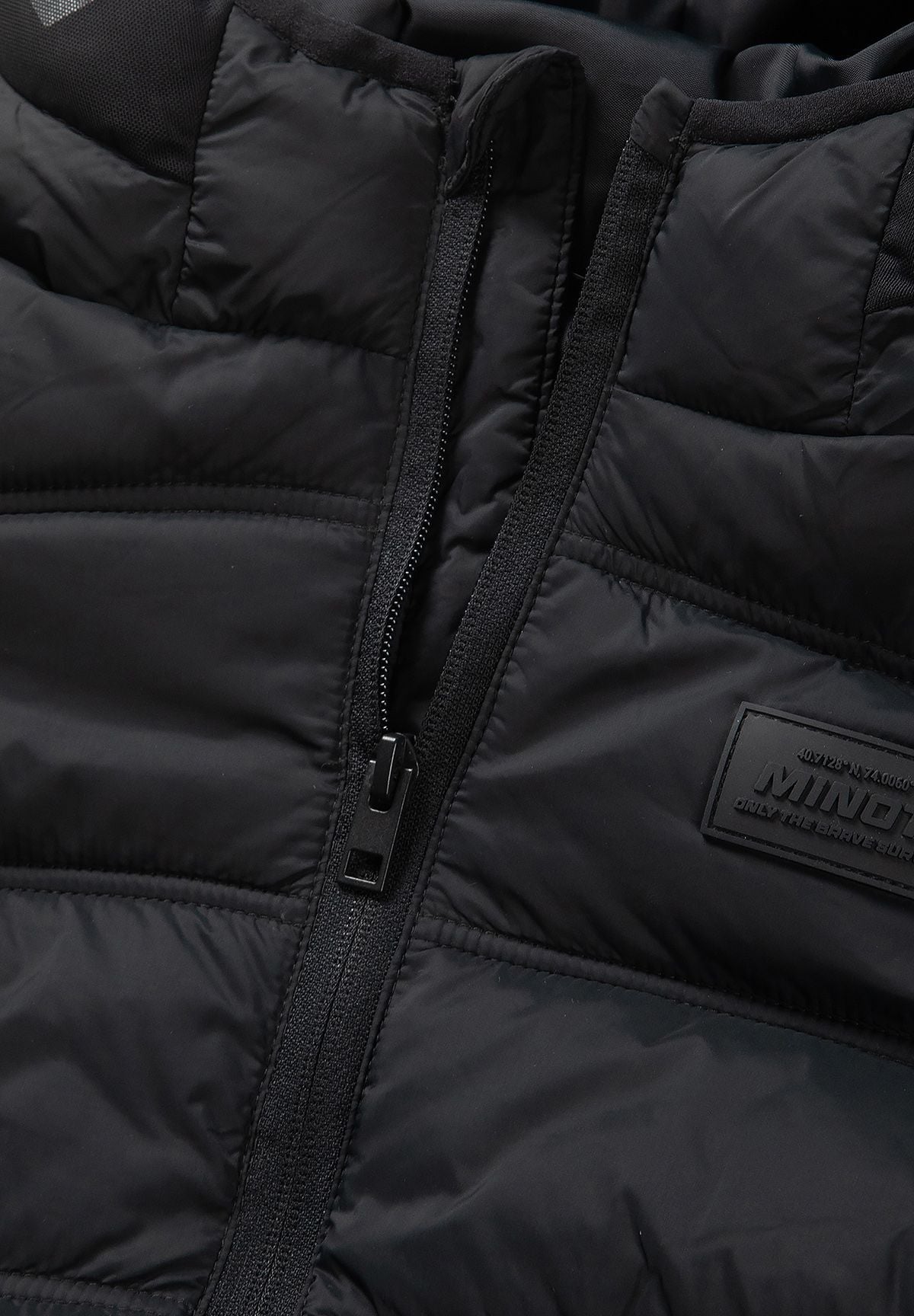 Close-up of the black jacket's upper zip with padded chin guard and tonal chest patch.