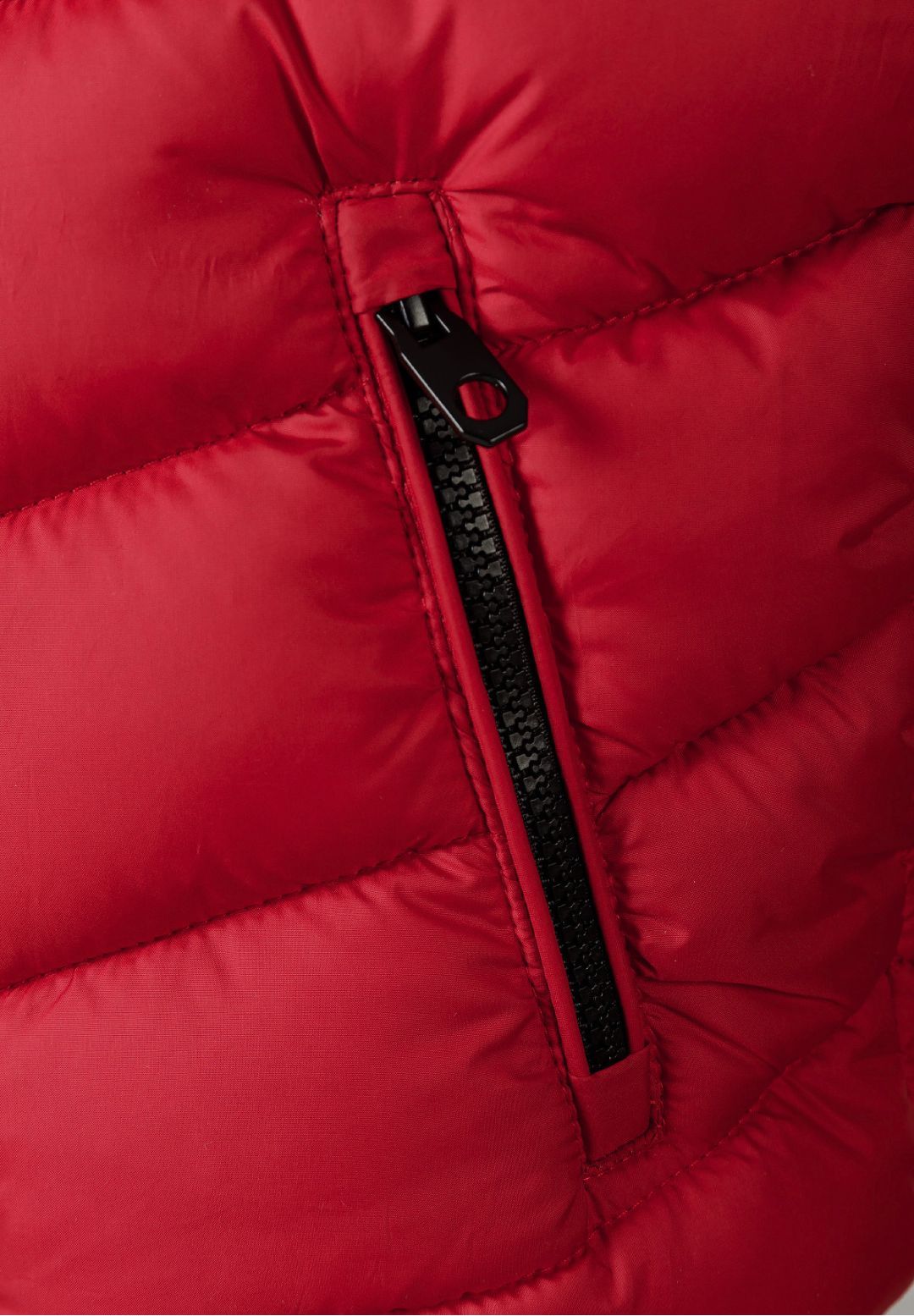 Close-up of a slanted black zipped side pocket on red quilted gilet fabric.