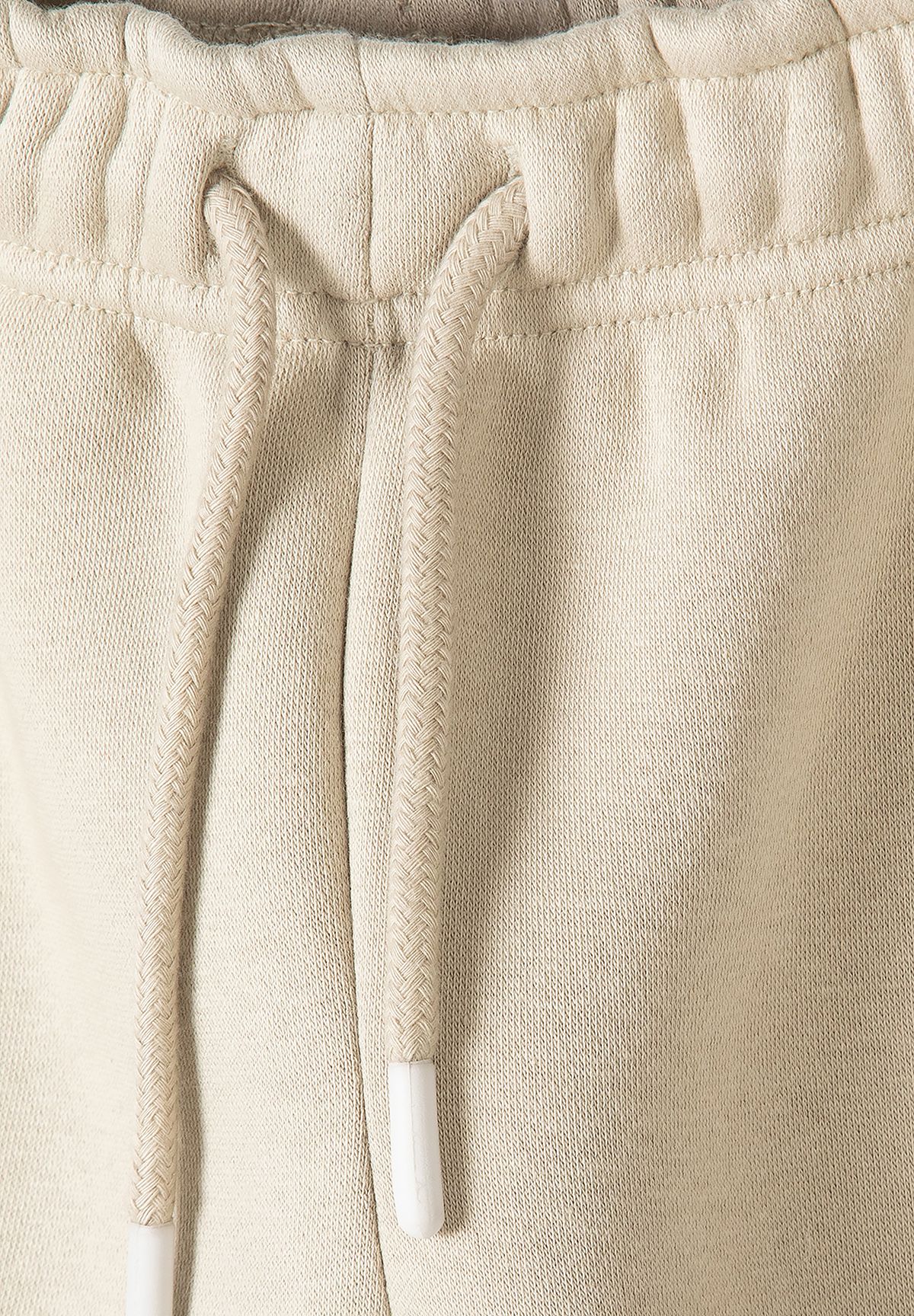 Close-up of cream joggers' gathered waistband and braided matching drawcord.