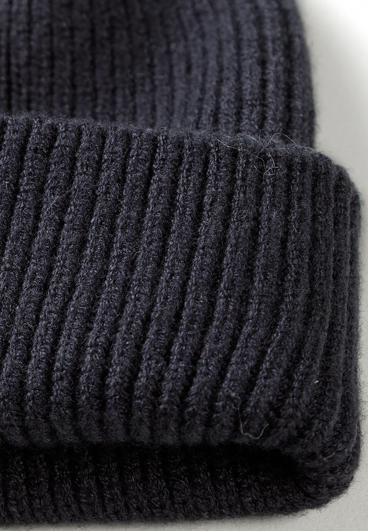 Close-up of the black beanie's thick folded rib-knit brim and vertical yarn texture.