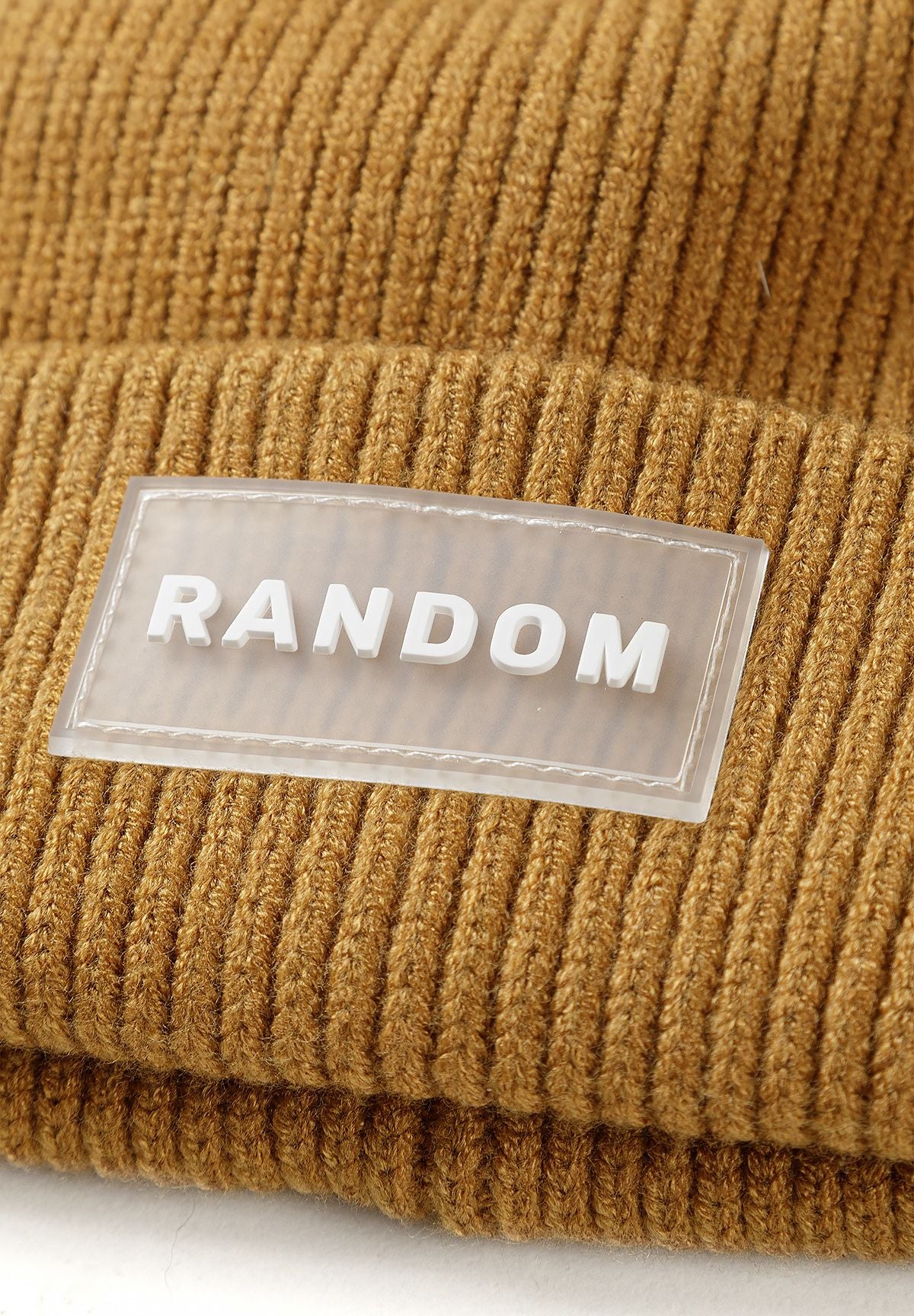 Close-up of translucent Random logo patch on ochre-brown beanie cuff.
