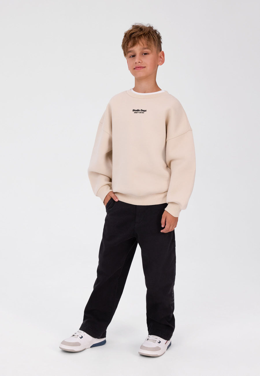 Boy wearing black relaxed carpenter trousers with a straight wide leg and a cream sweatshirt
