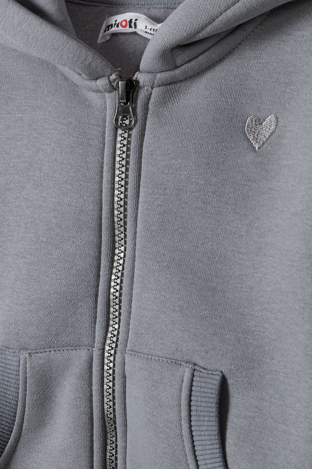 Close-up of grey hoodie's stitched heart beside the front zip and pouch pockets.