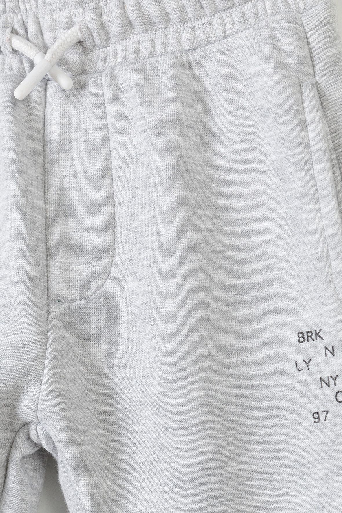 Close-up of grey jogger waistband, pocket and small black thigh print.