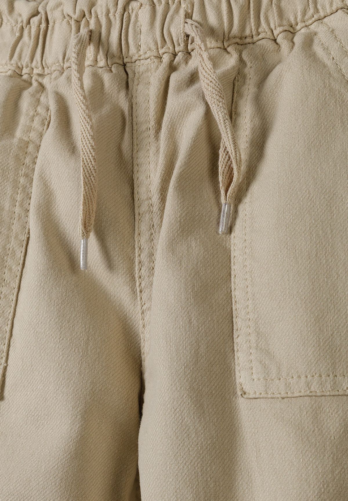 Close-up of beige paperbag waist, drawcord and front patch pocket.