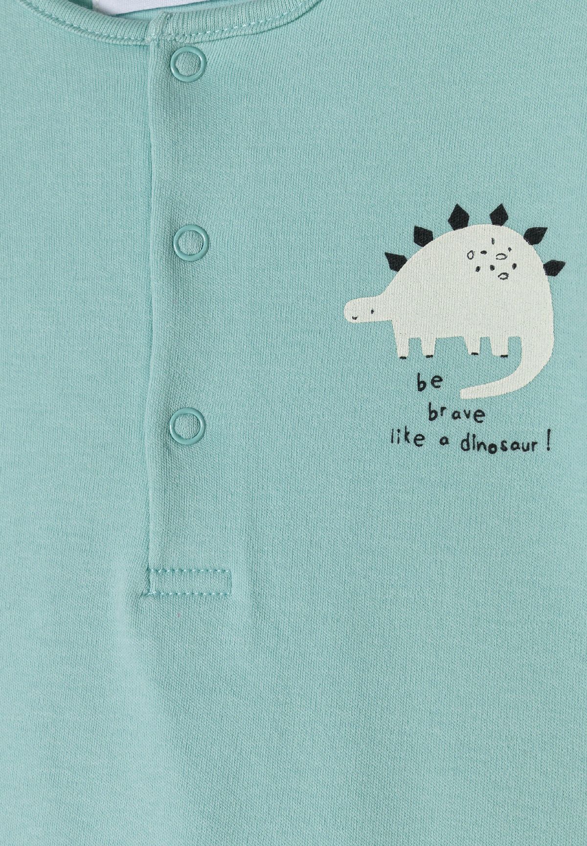 Close-up of mint romper's three studs and white dinosaur print with Be Brave text.