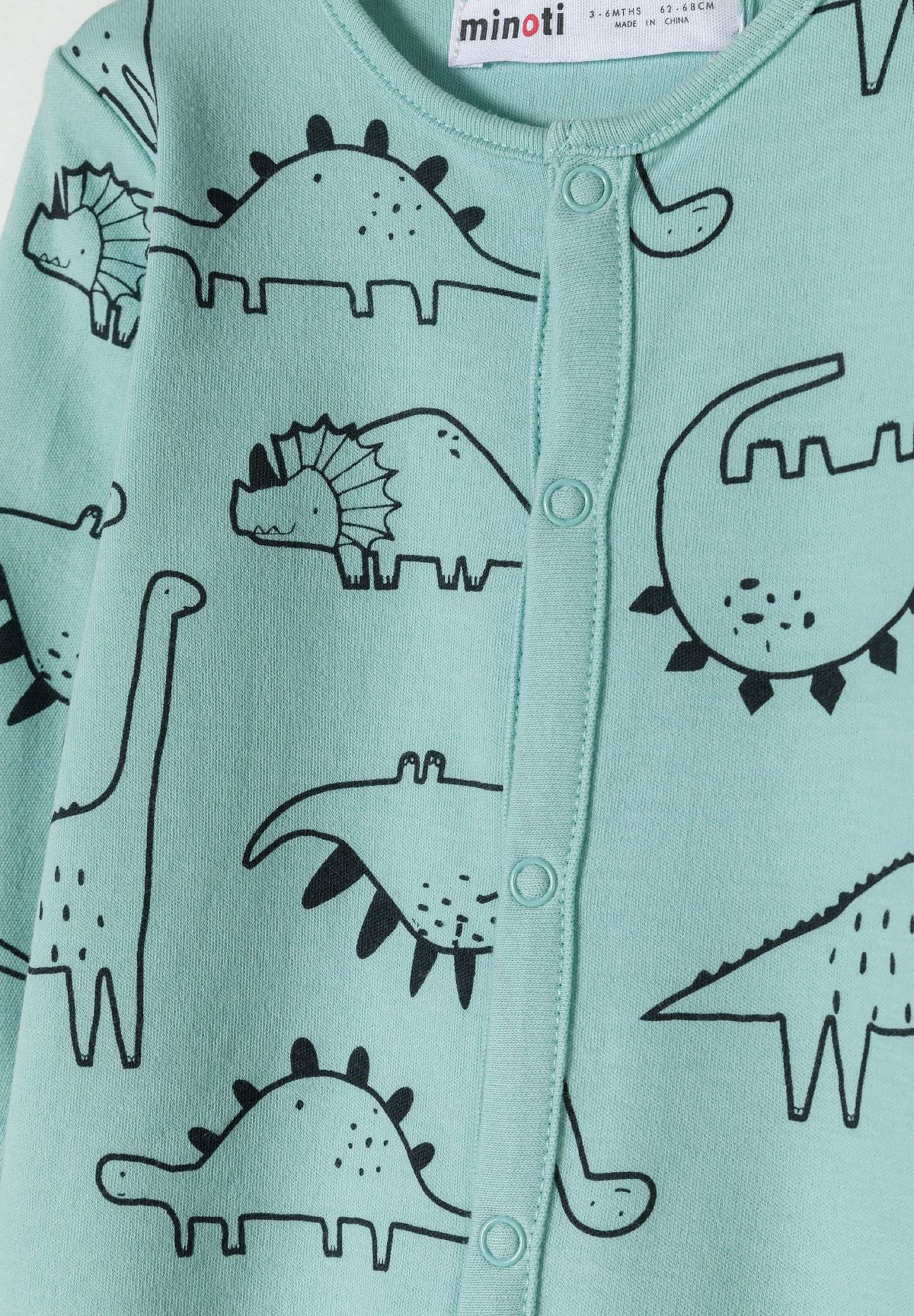 Close-up of mint sleepsuit poppers beside black dinosaur drawings.
