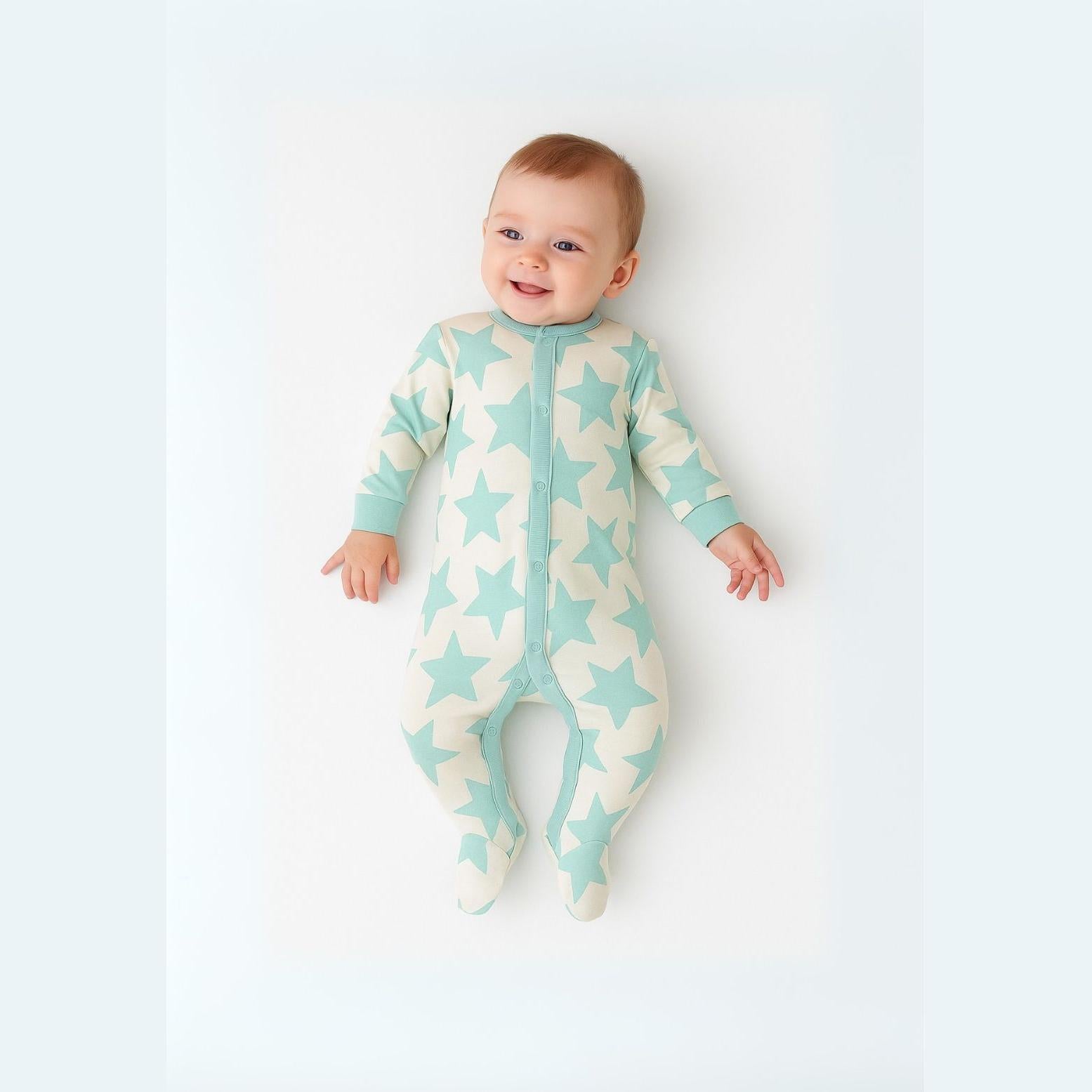 Smiling baby wearing mint green star print sleepsuit lying on white surface