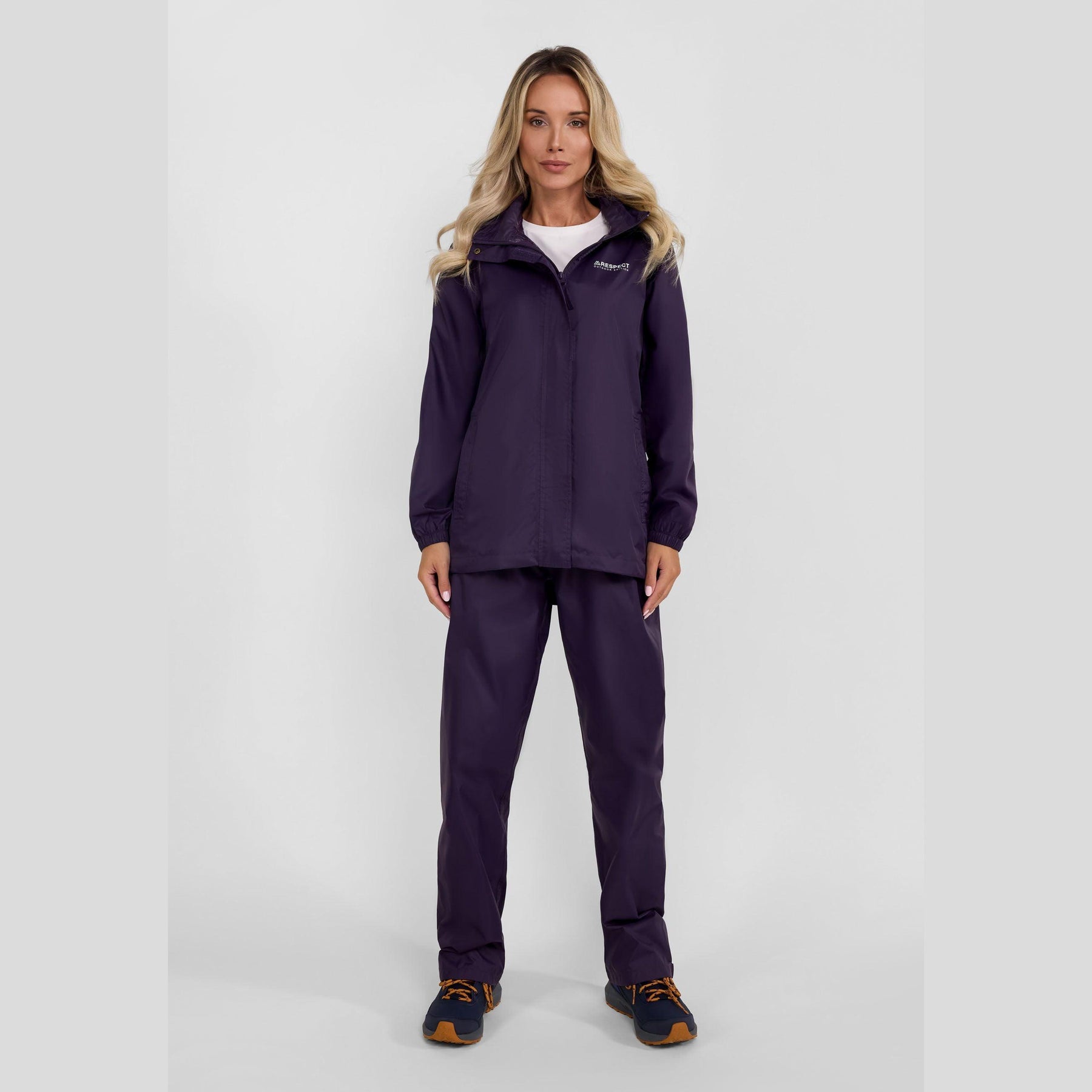 Woman wearing purple waterproof overpants and jacket set standing against white background, full body view showing complete rain protection outfit