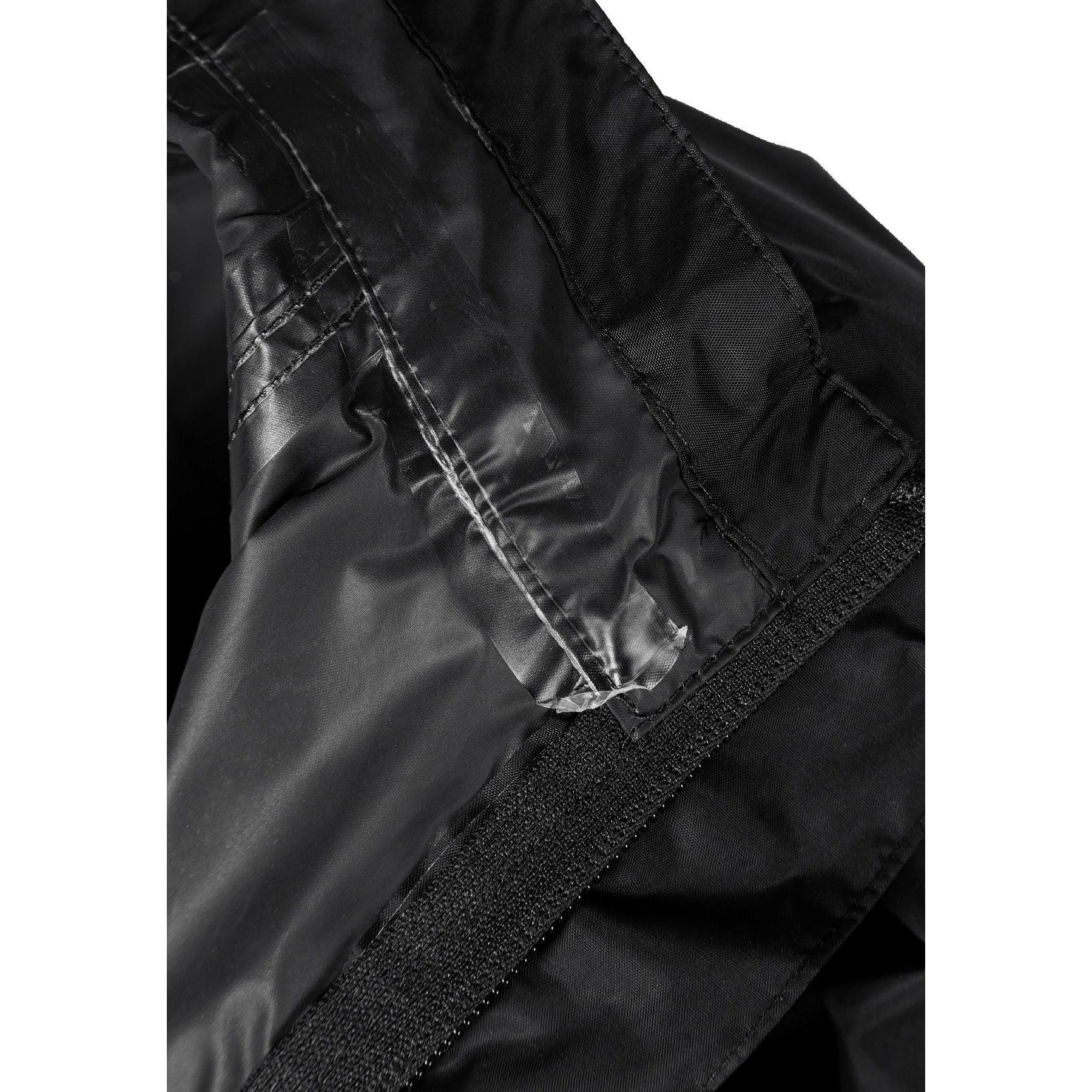 Boy in black hooded waterproof jacket pointing forward, wearing light blue cargo jeans and black sneakers on white studio background