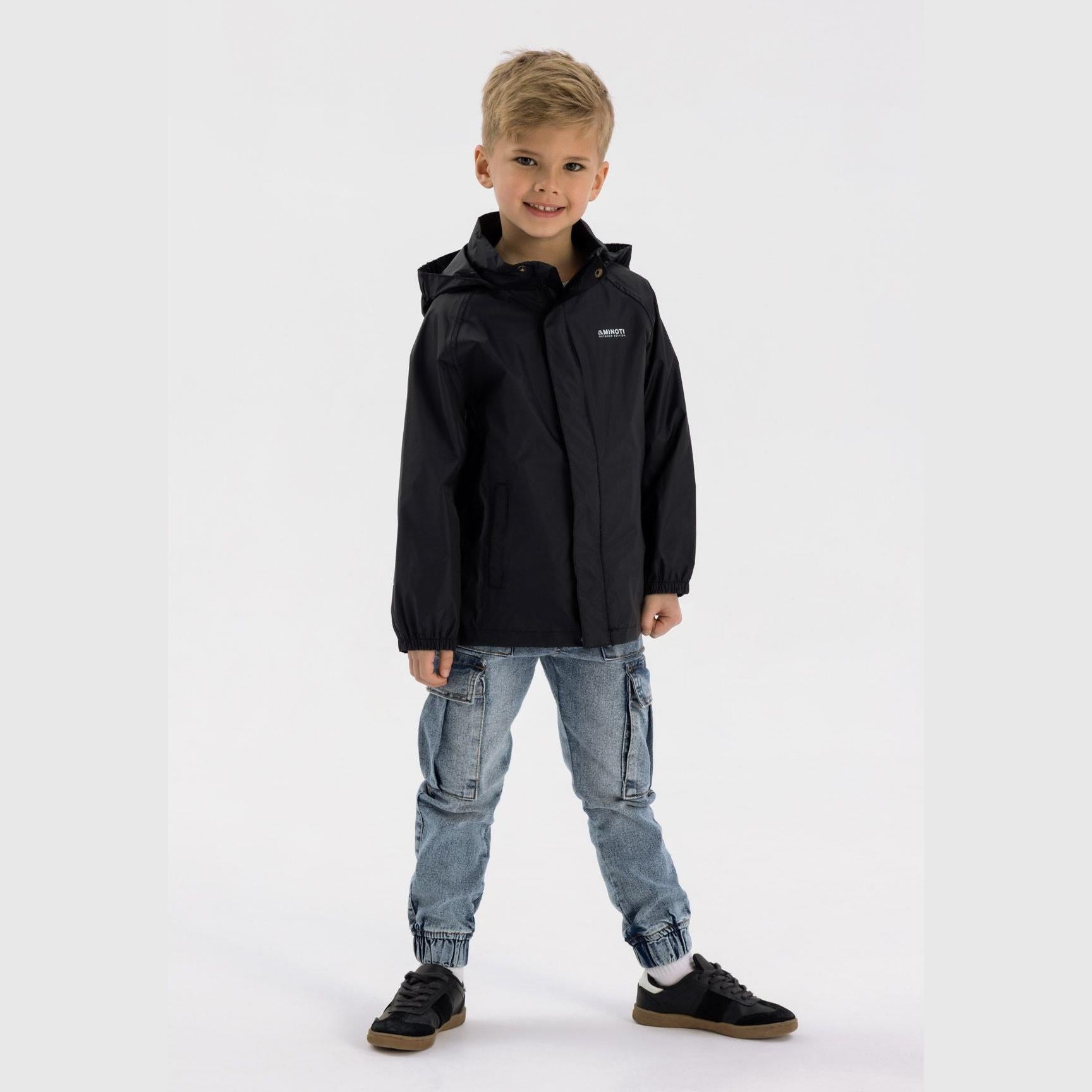 Boy in black hooded waterproof jacket pointing forward, wearing light blue cargo jeans and black sneakers on white studio background