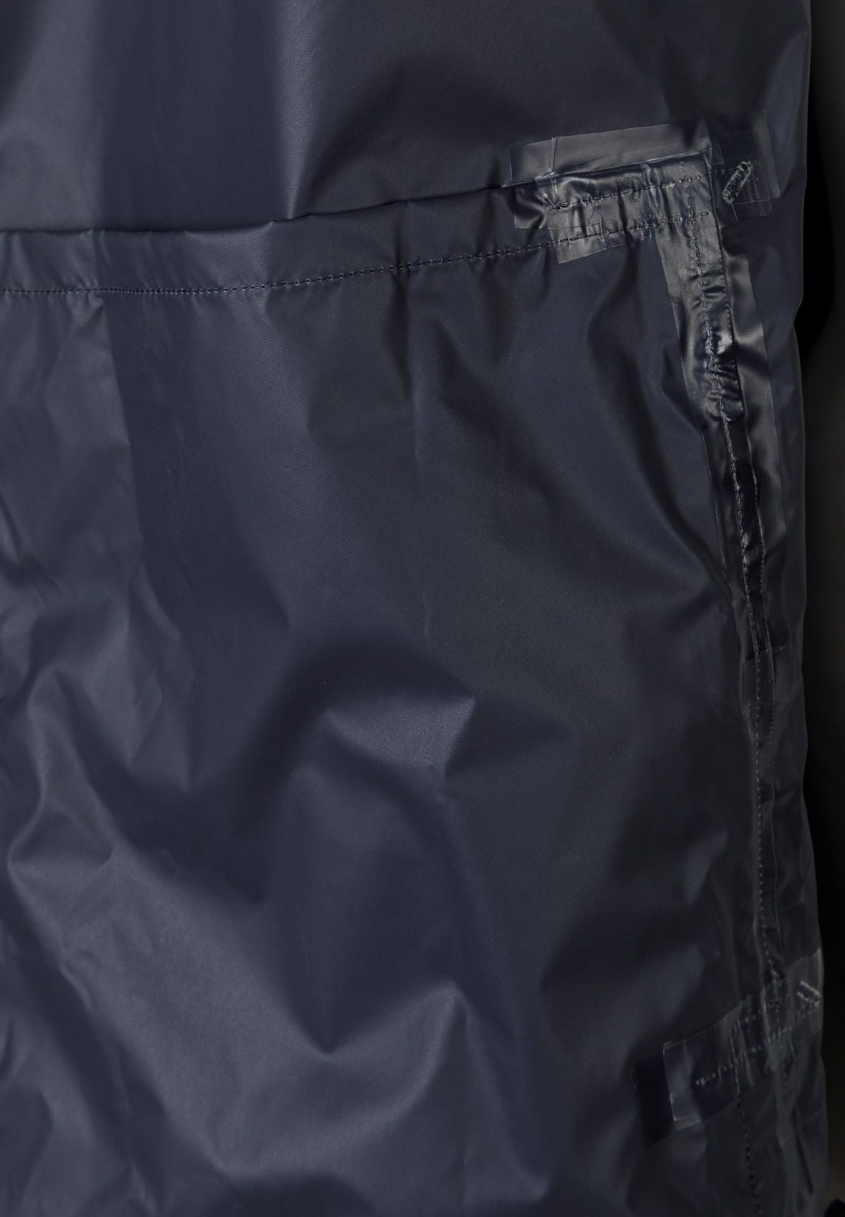 Detail of navy waterproof jacket with zip pocket and pleated flap.