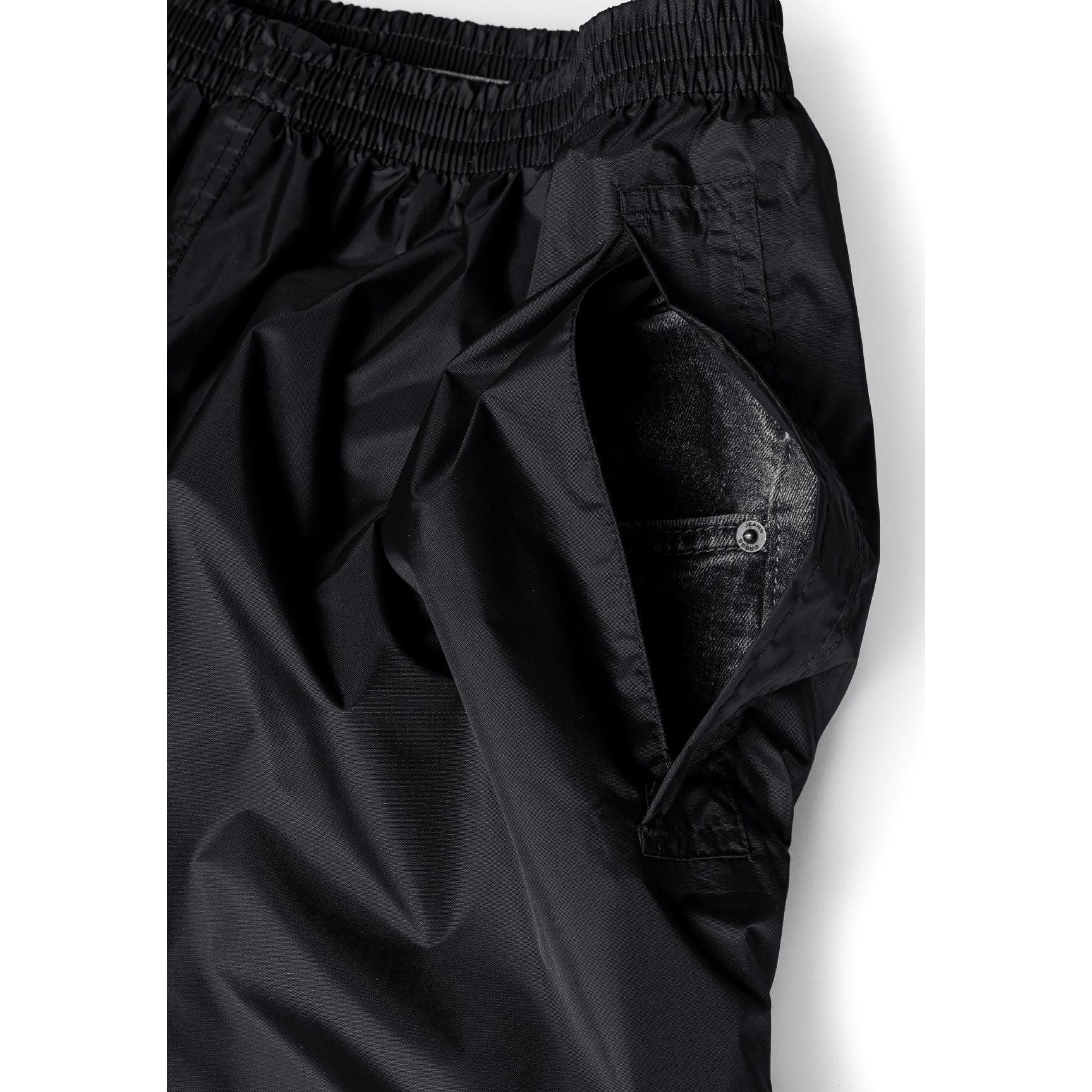 Close-up detail of black waterproof overpants showing side pocket with button closure and adjustable hem with snap fastener