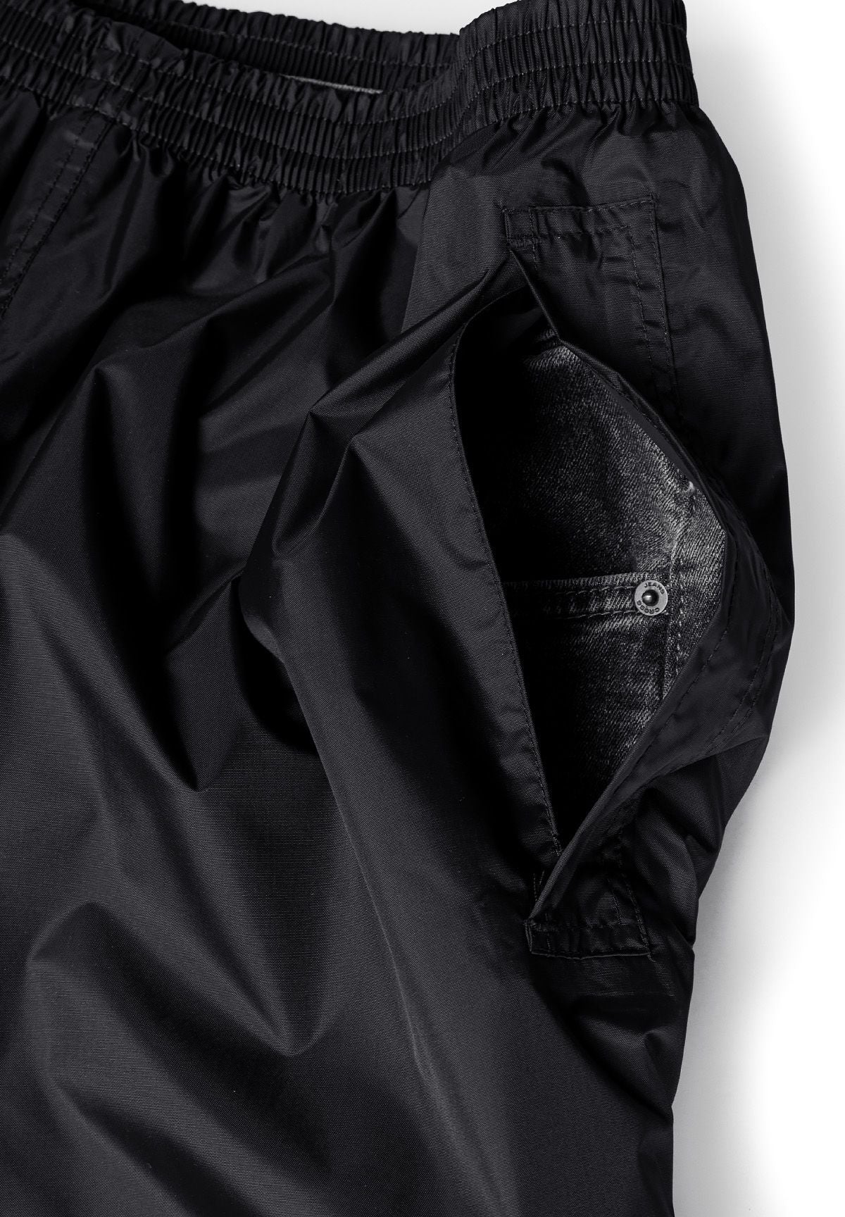 Close-up of black waterproof overpants with elasticated waistband and side pocket access.