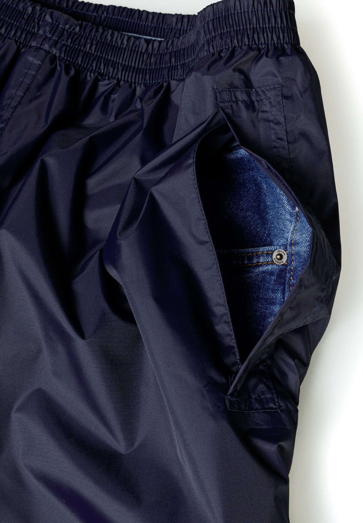 Close-up of navy waterproof overpants with elastic waistband and side pocket opening.