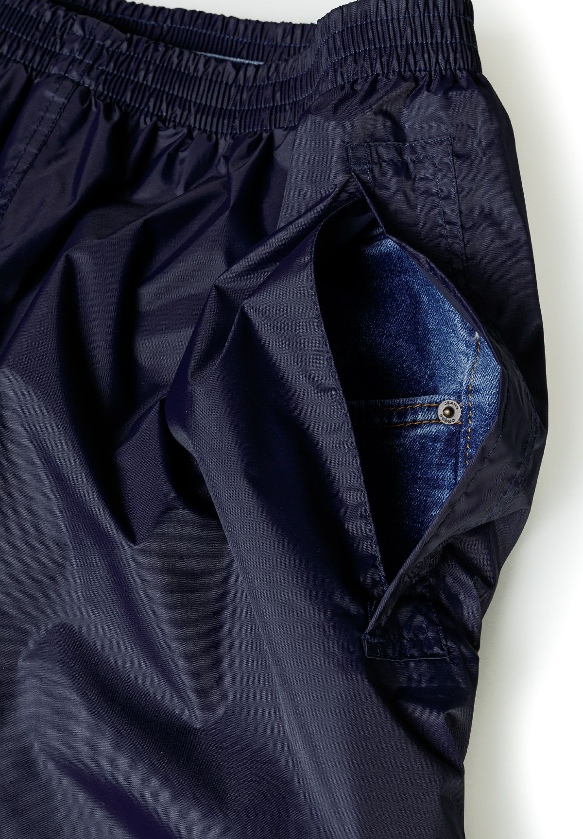 Open side access slit in navy overtrousers revealing a jeans pocket underneath.