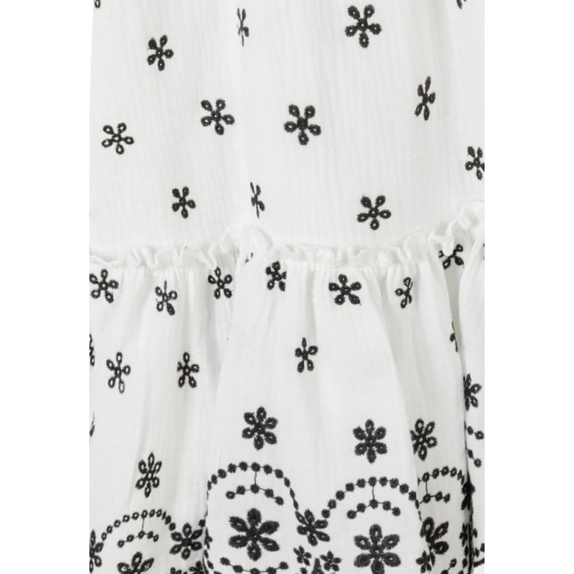 Close-up detail of cream dress fabric showing black embroidered floral motifs and decorative scalloped hem border with intricate stitching