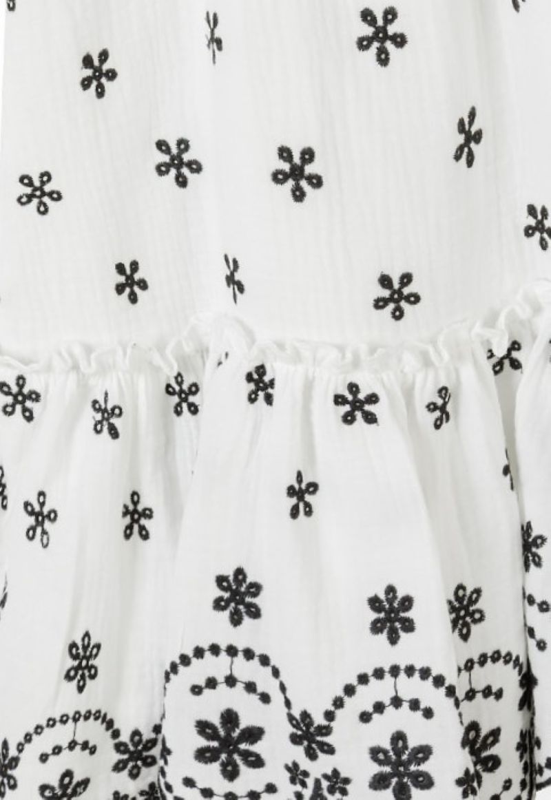Close-up of black embroidered flowers and scalloped floral border on white sundress.