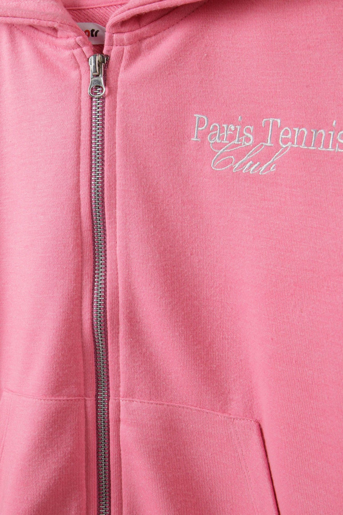 Close-up of silver zip and pale Paris Tennis Club lettering on pink hoodie chest.