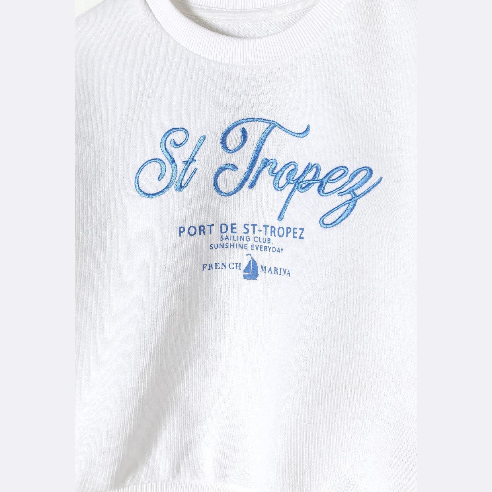 Close-up detail of white sweatshirt showing blue St Tropez Port de St-Tropez sailing club print with French marina text and sailboat graphic