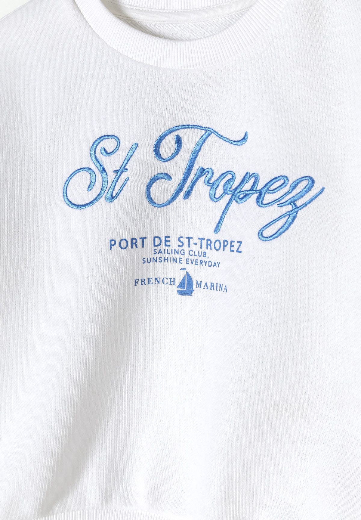 Close-up of a white girls fleece crew neck sweatshirt with blue decorative print.