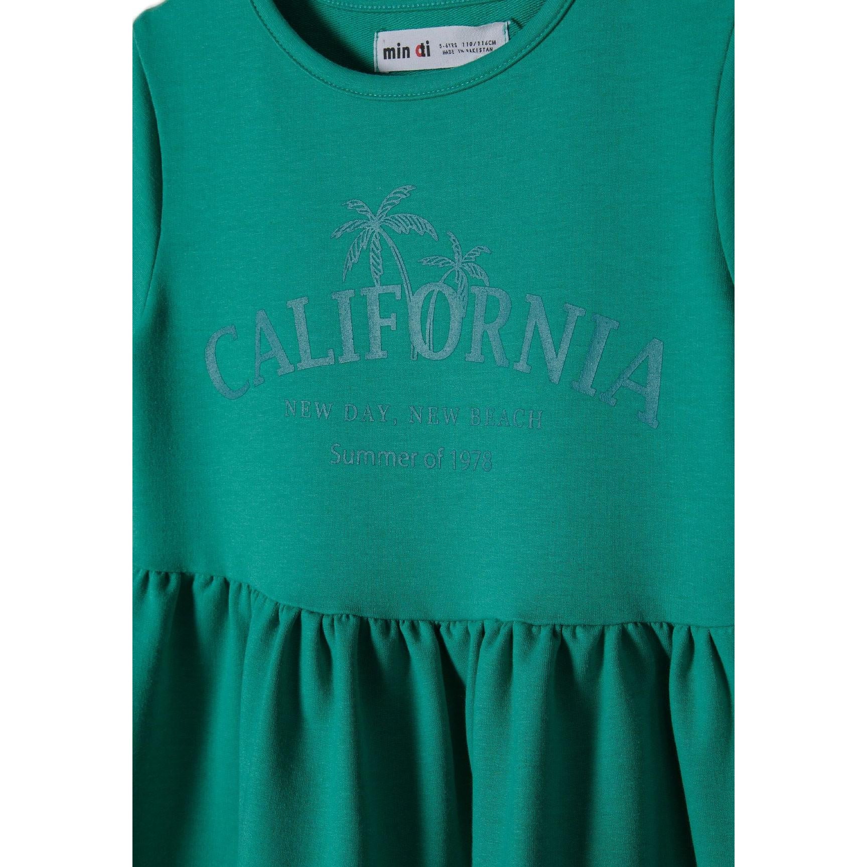 Close-up detail of green dress showing Minoti label and California palm tree print with 'New Day New Dream Summer of Joy' text