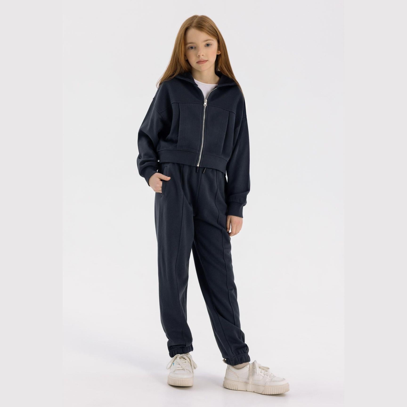 Girl wearing navy tracksuit set with cropped zip hoodie and joggers against white background