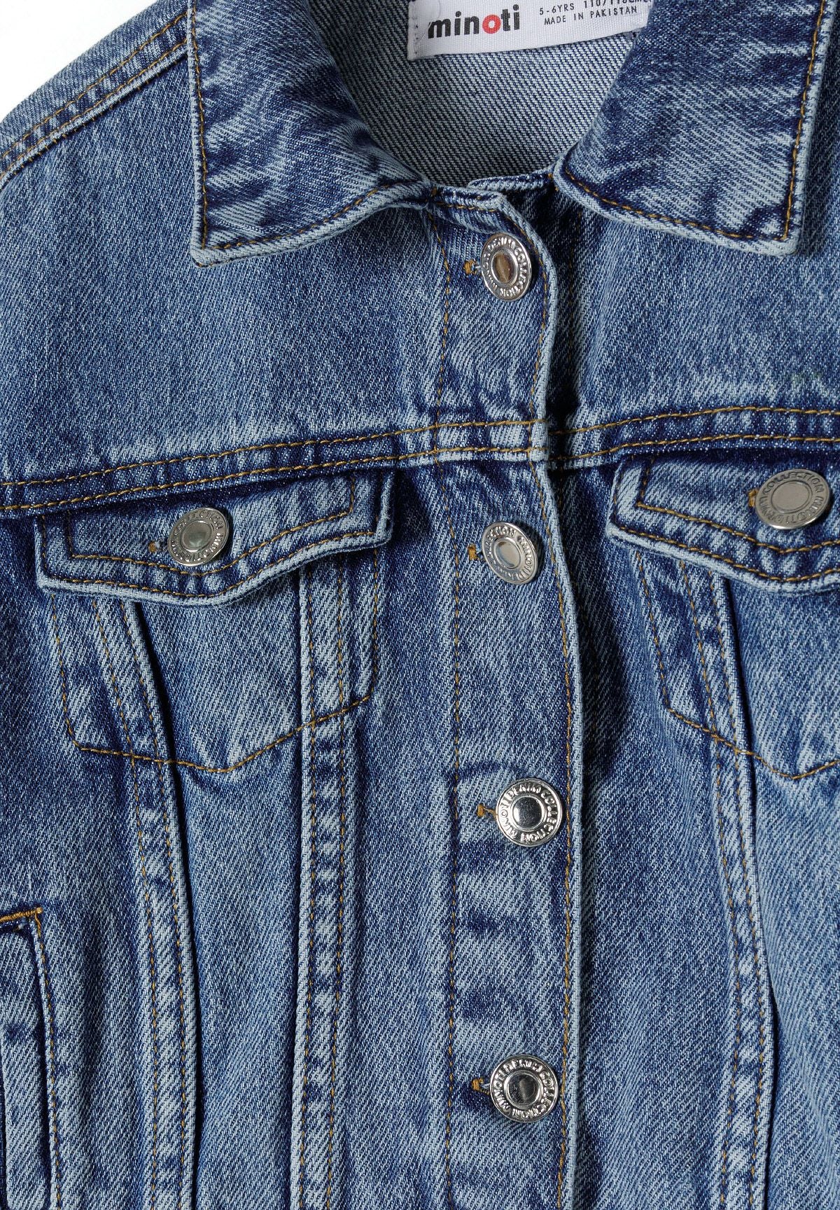 Detail of a girls' oversized denim jacket in blue with buttoned chest pockets and collar.